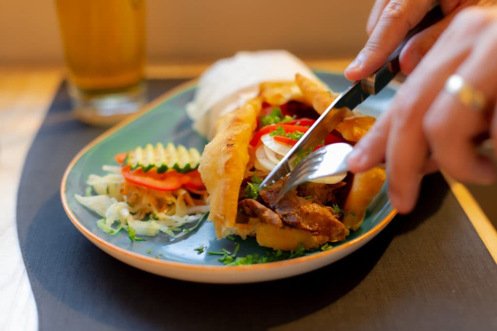 Die Hände einer Person schneiden mit Messer und Gabel ein griechisches Gericht.