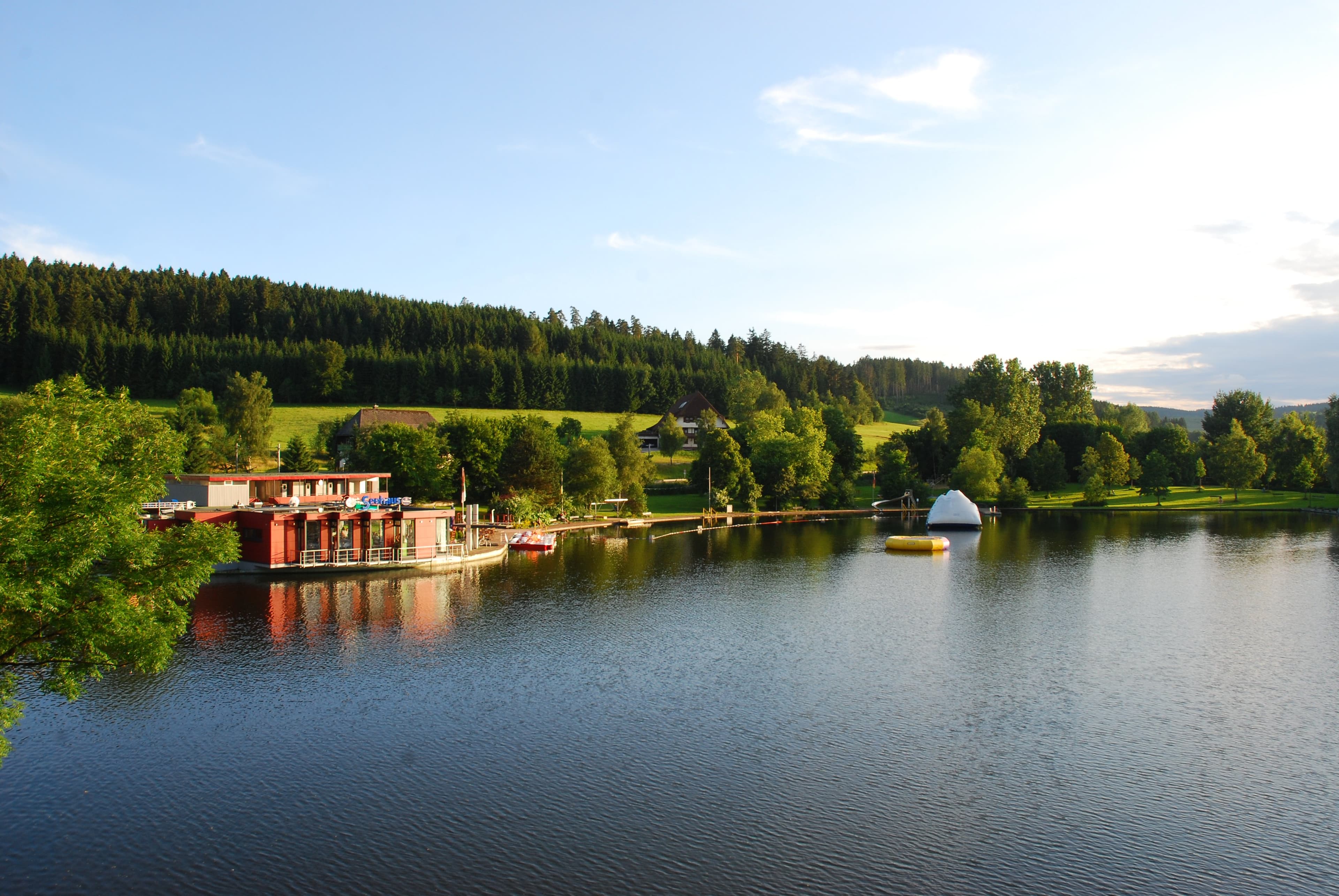 A lake with an adjoining restaurant, and trees and meadows in the background