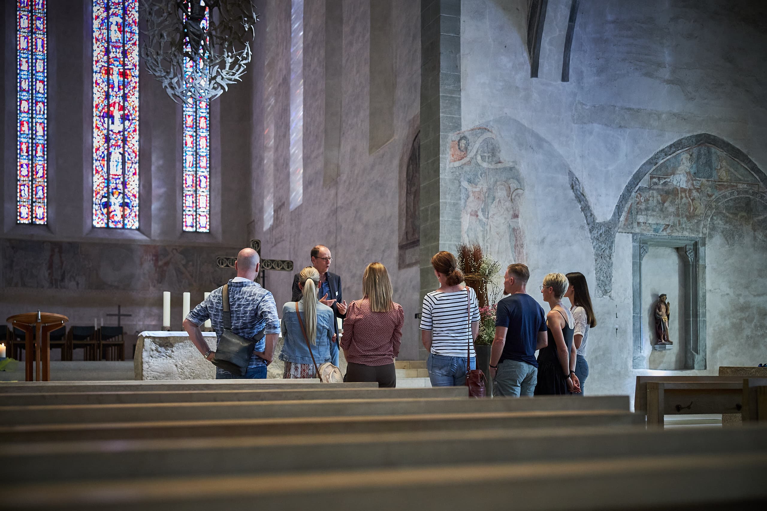 A group of people in a church with colorful windows and murals.
