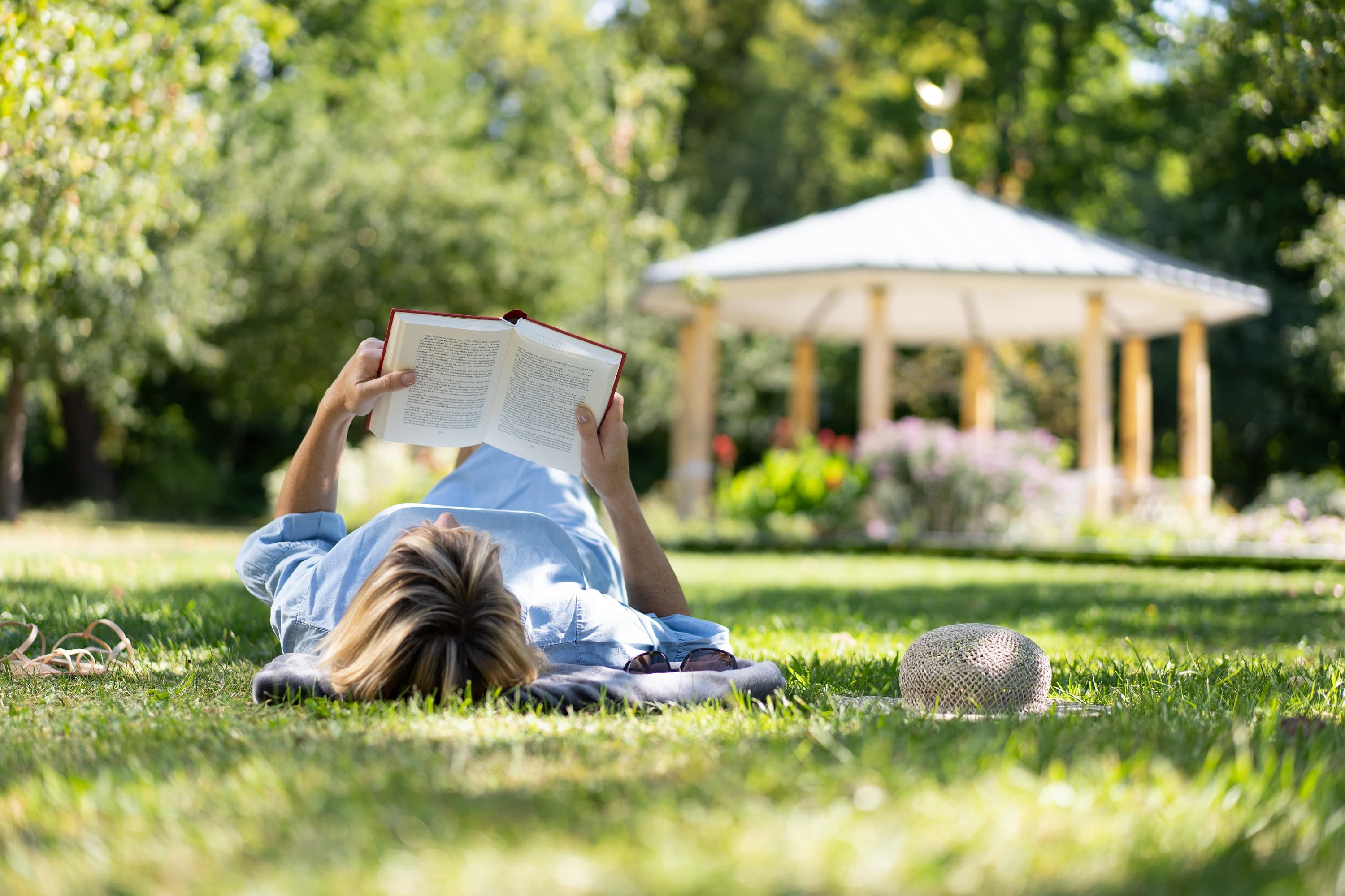 Eine Frag liegt mit auf der Wiese im Schlosspark und liest ein Buch.