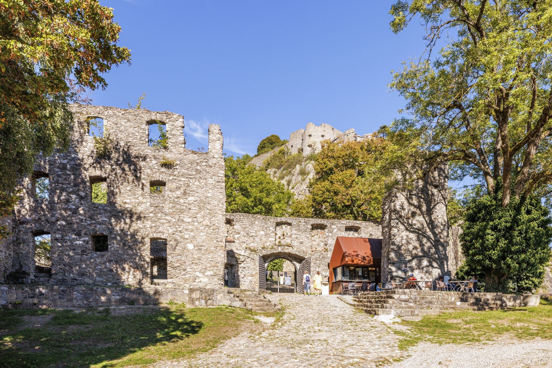 Ruins of an old castle with stone walls and an entrance, people and tables outside.