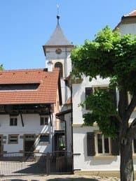 Weißer Kirchturm mit Uhr hinter Häusern unter blauem Himmel