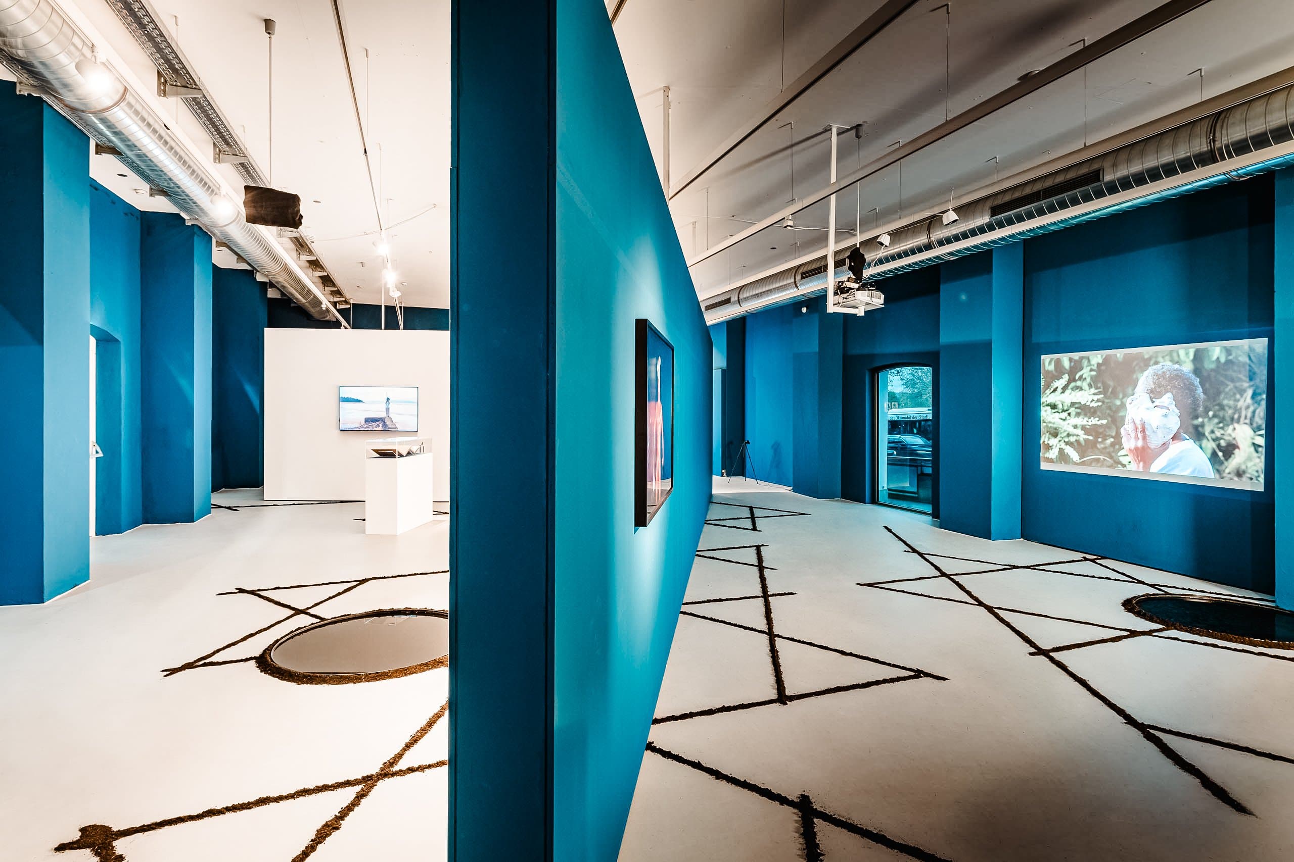 Moderne Galerie mit blauen Wänden und Videoinstallationen.
