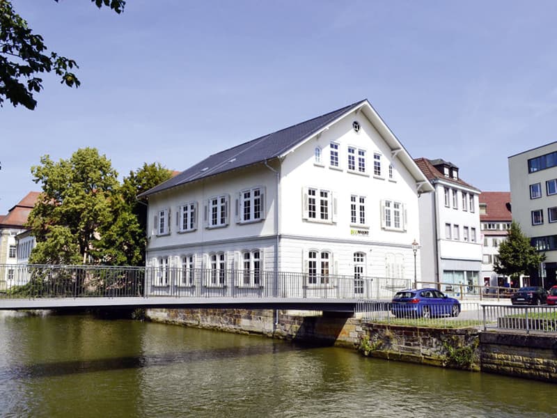 Ein weißes Gebäude an einem Fluss mit Brücke und blauen Himmel.