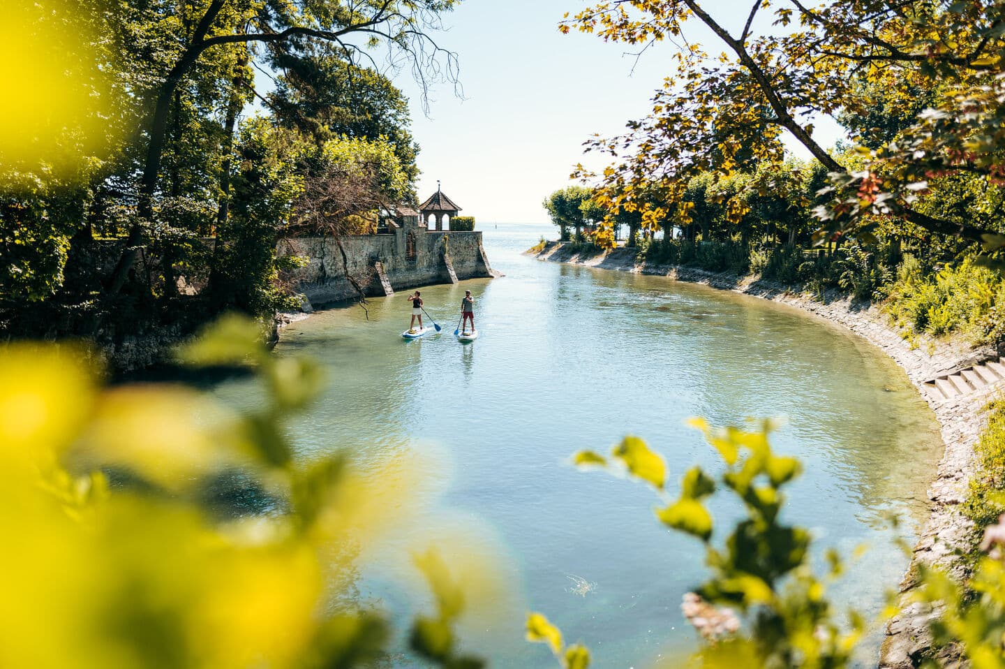 Im Konstanzer Stadtgarten mit Blick auf den Bodensee. Zwei Personen befinden sich mit SUP auf dem Wasser.