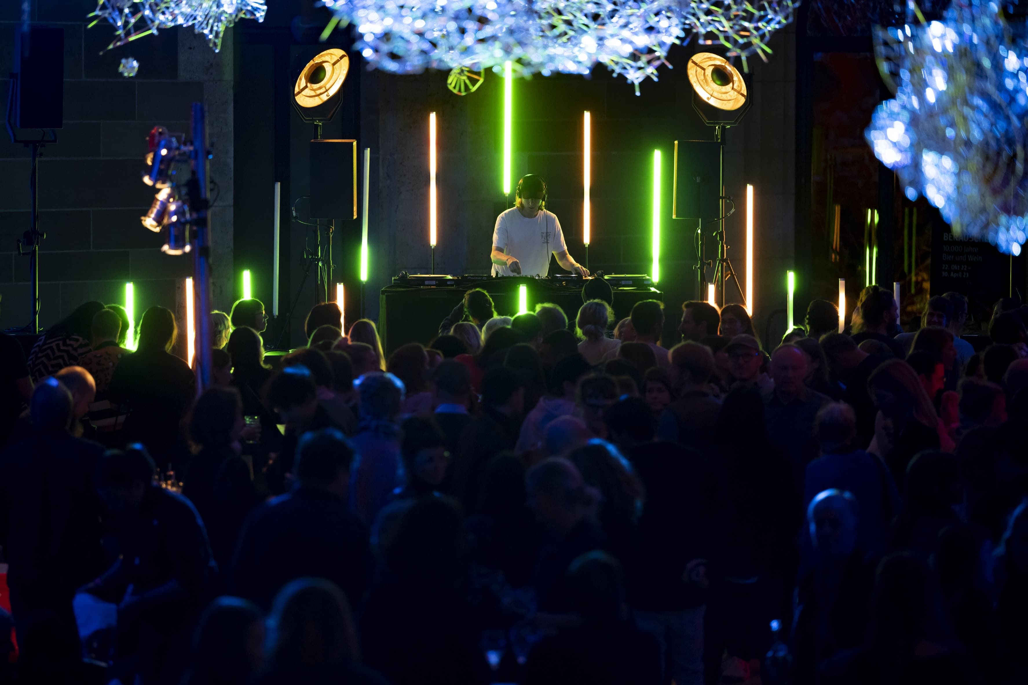 DJ vor grün beleuchteter Kulisse und Publikum