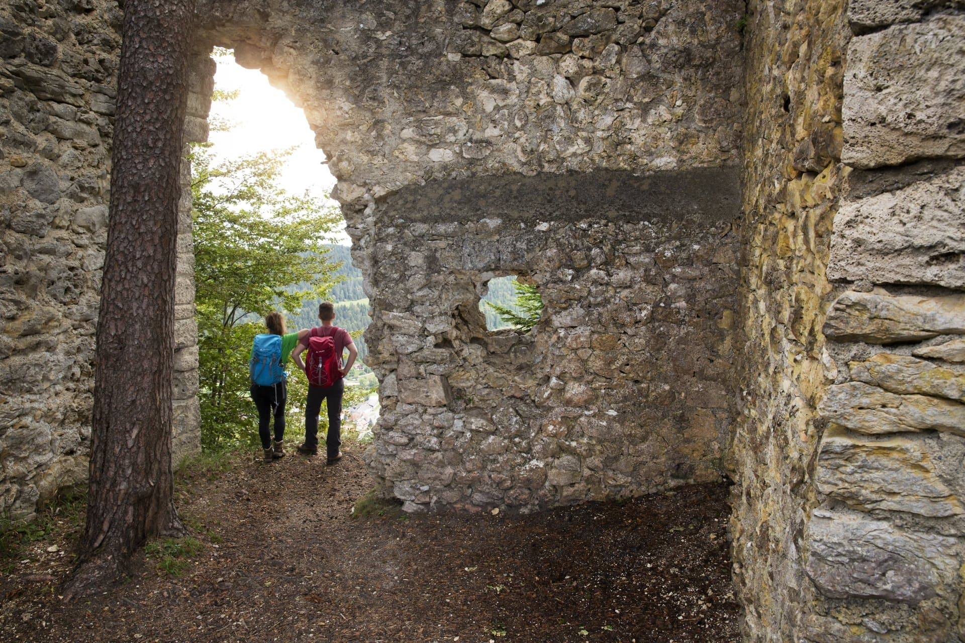 Ein Paar steht in einem Durchgang zwischen den steinigen Mauern der Ruine Granegg und schaut in die Landschaft.