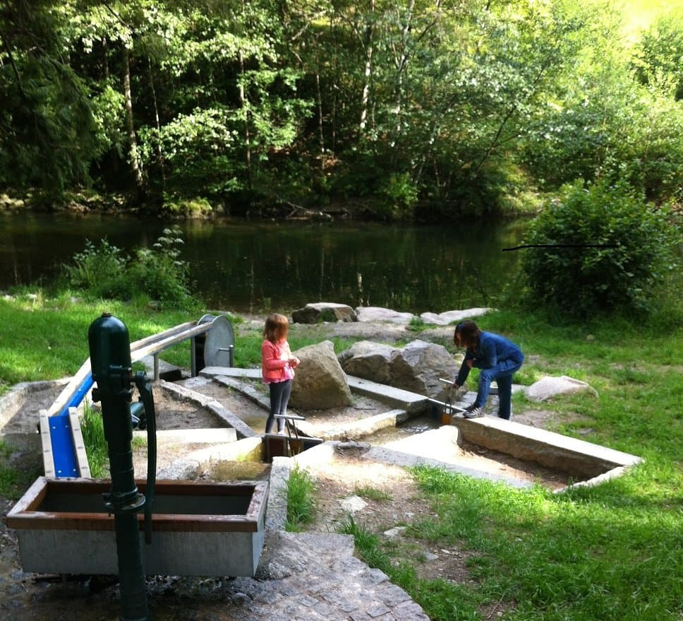 Zwei Kinder beim spielen an der Wasserpumpe und am Wasserlauf an der Wiese im Energieerlebnispfad Buchenbrändle