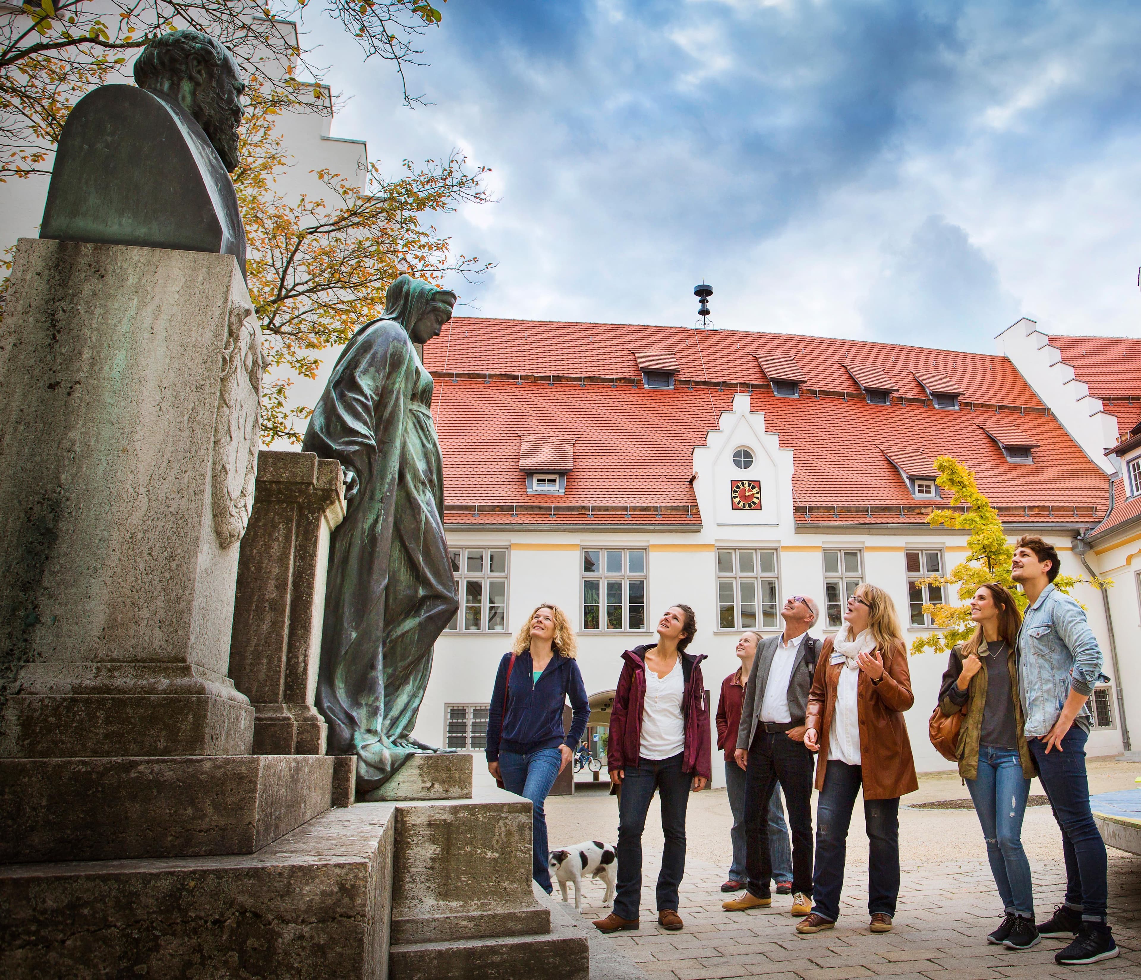 Eine Stadtführungsgruppe betrachtet eine Bronzestatue vor dem Biberacher Spital.