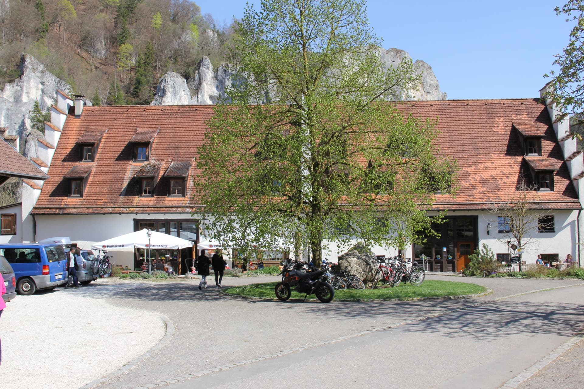 Ein längliches Gebäude mit Staffelgiebel, davor ein Rondell mit einem Solitärbaum und verschiedenen Fahrzeugen