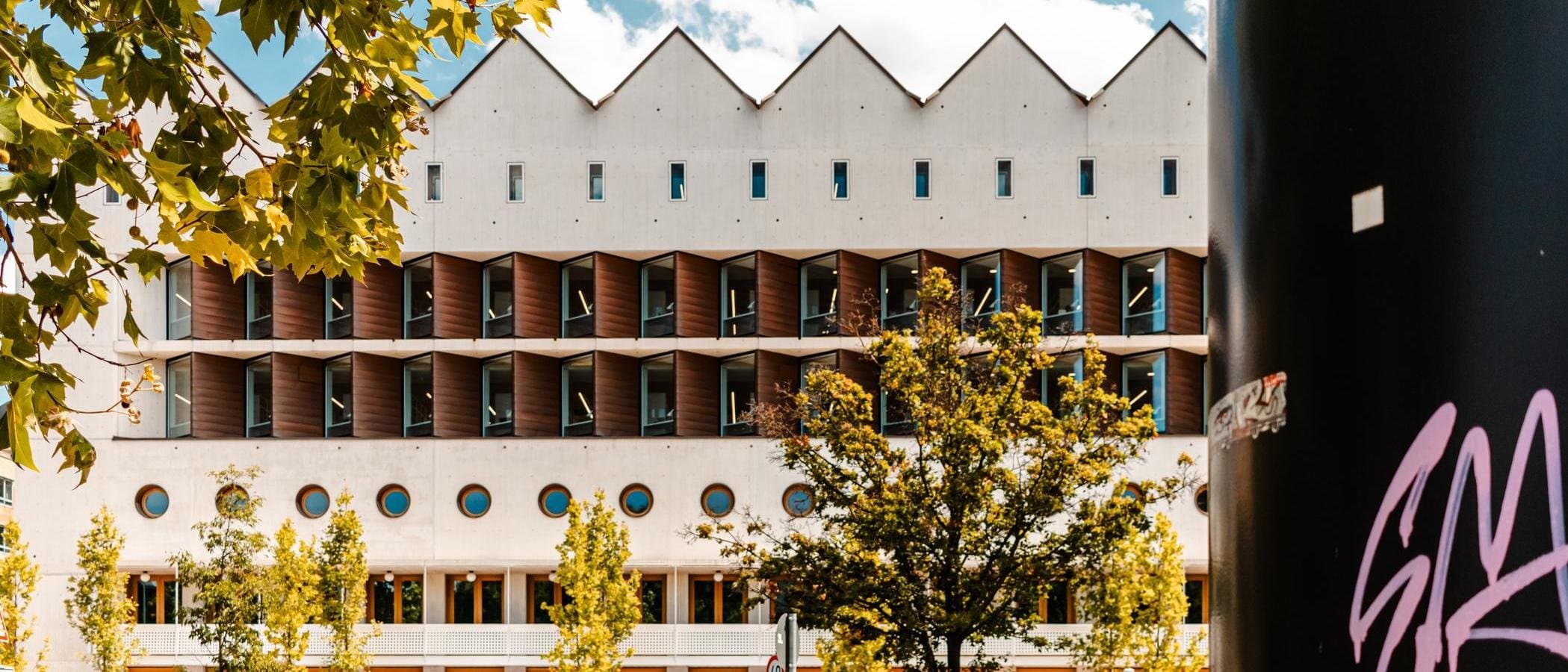 Moderne Bibliothek mit geometrischer Fassade und Bäumen im Vordergrund.