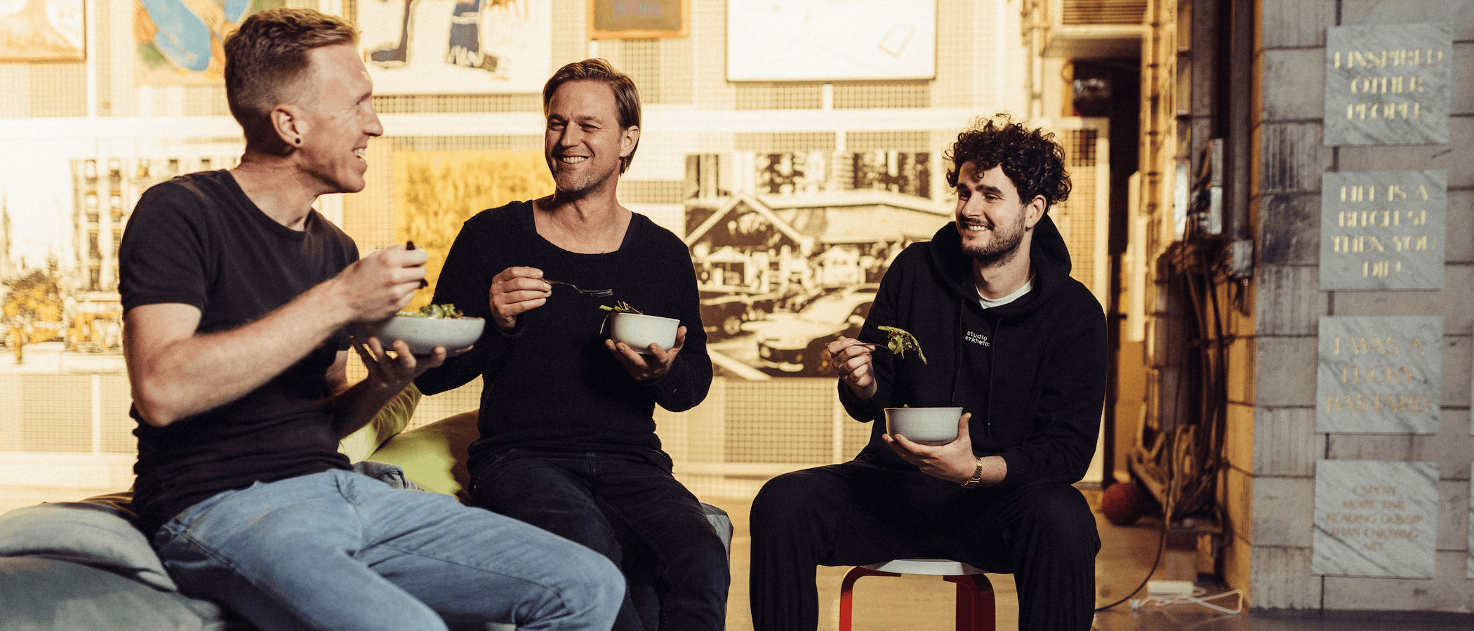 Drei Männer sitzen und essen Salat in einem gemütlichen Raum.