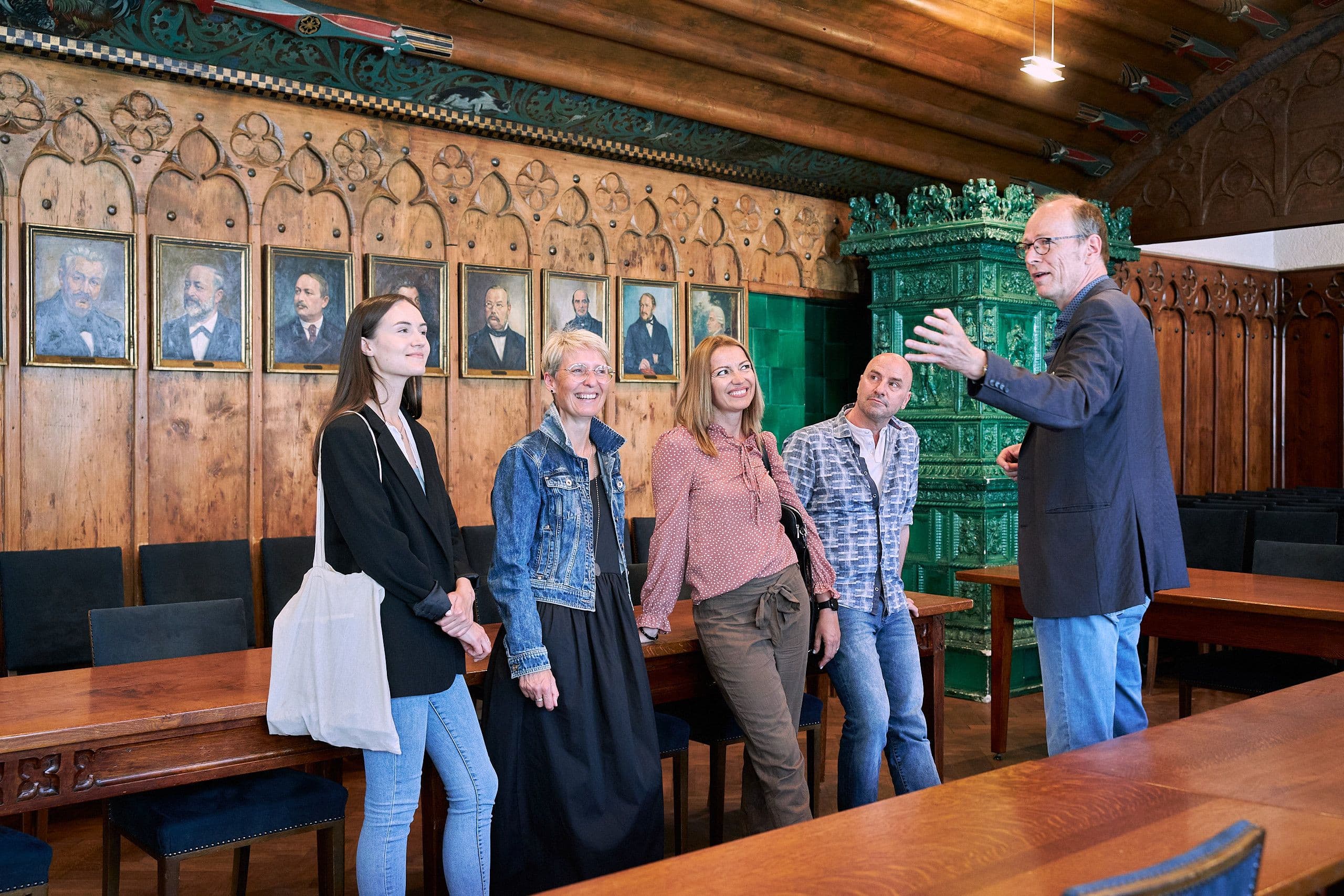 A group of people in a wood-paneled room with portraits on the wall.  The city guide talks about the witch trials in Ravensburg.
