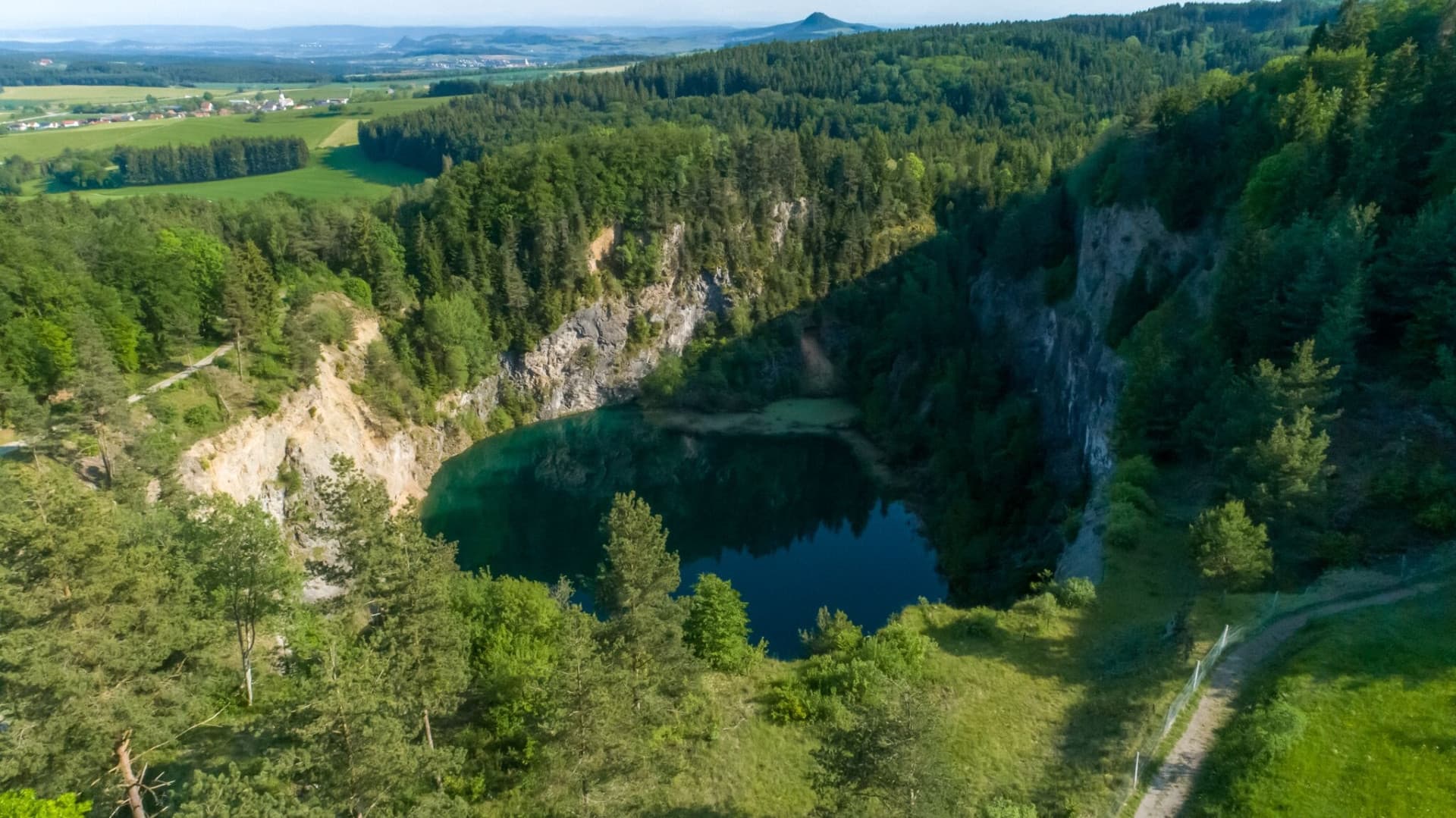 Luftsansicht auf einen von Felsen und Wald umgebenen kleinen See.
