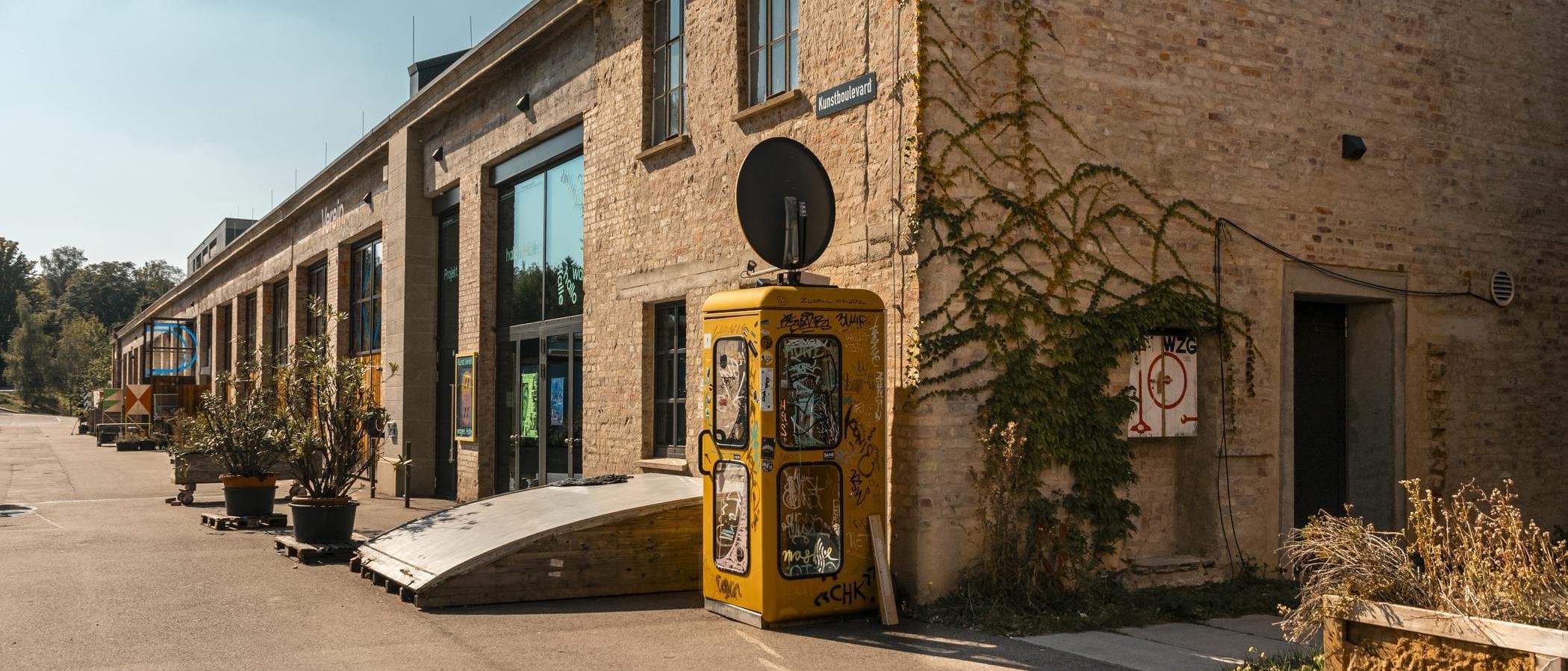 Altes Backsteingebäude mit gelber Telefonzelle und Pflanzen.