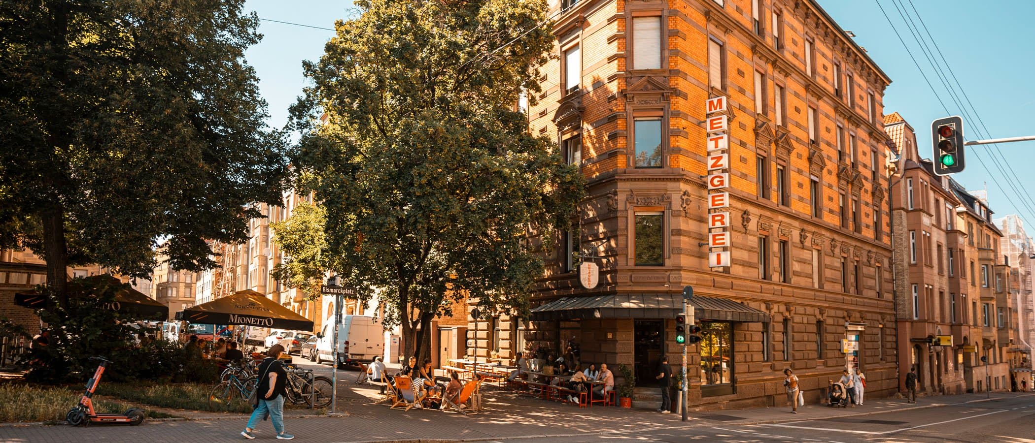 Straßenszene am Bismarckplatz mit Metzgerei und Cafégästen.