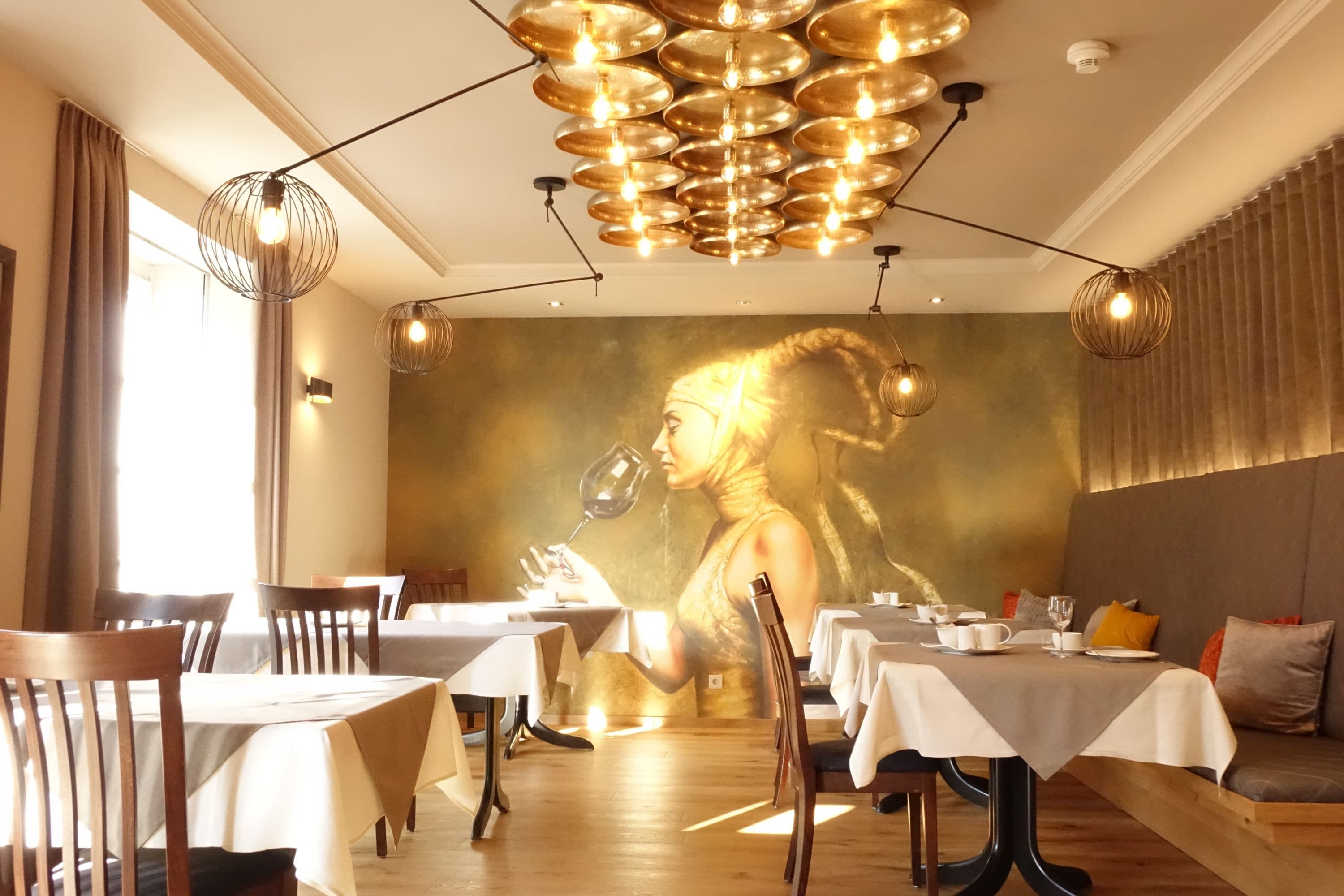 Breakfast room with a golden picture of a woman in the background. There is a bench with cushions on the right and tables by the window on the left.