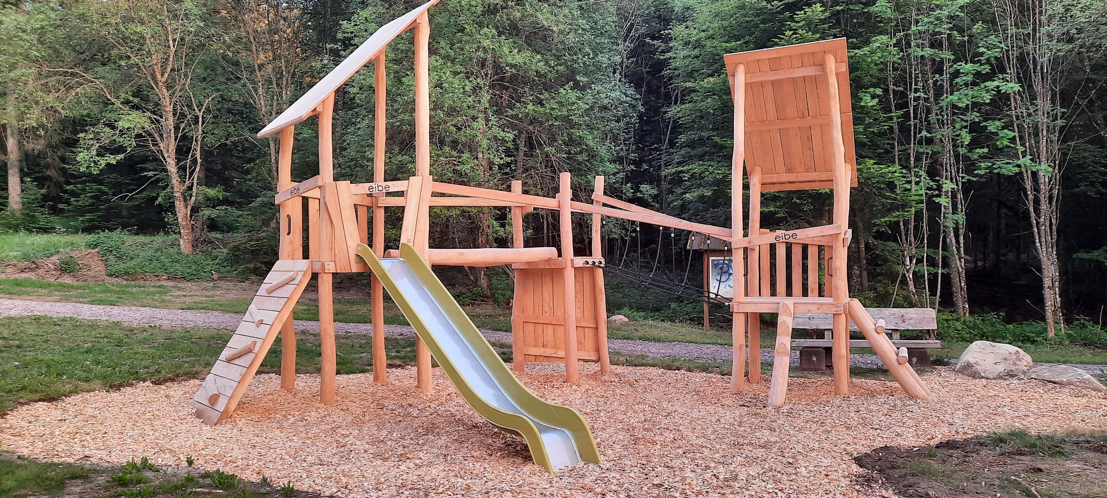 Holzkletterspielplatz mit Rutsche im Wald gelegen.
