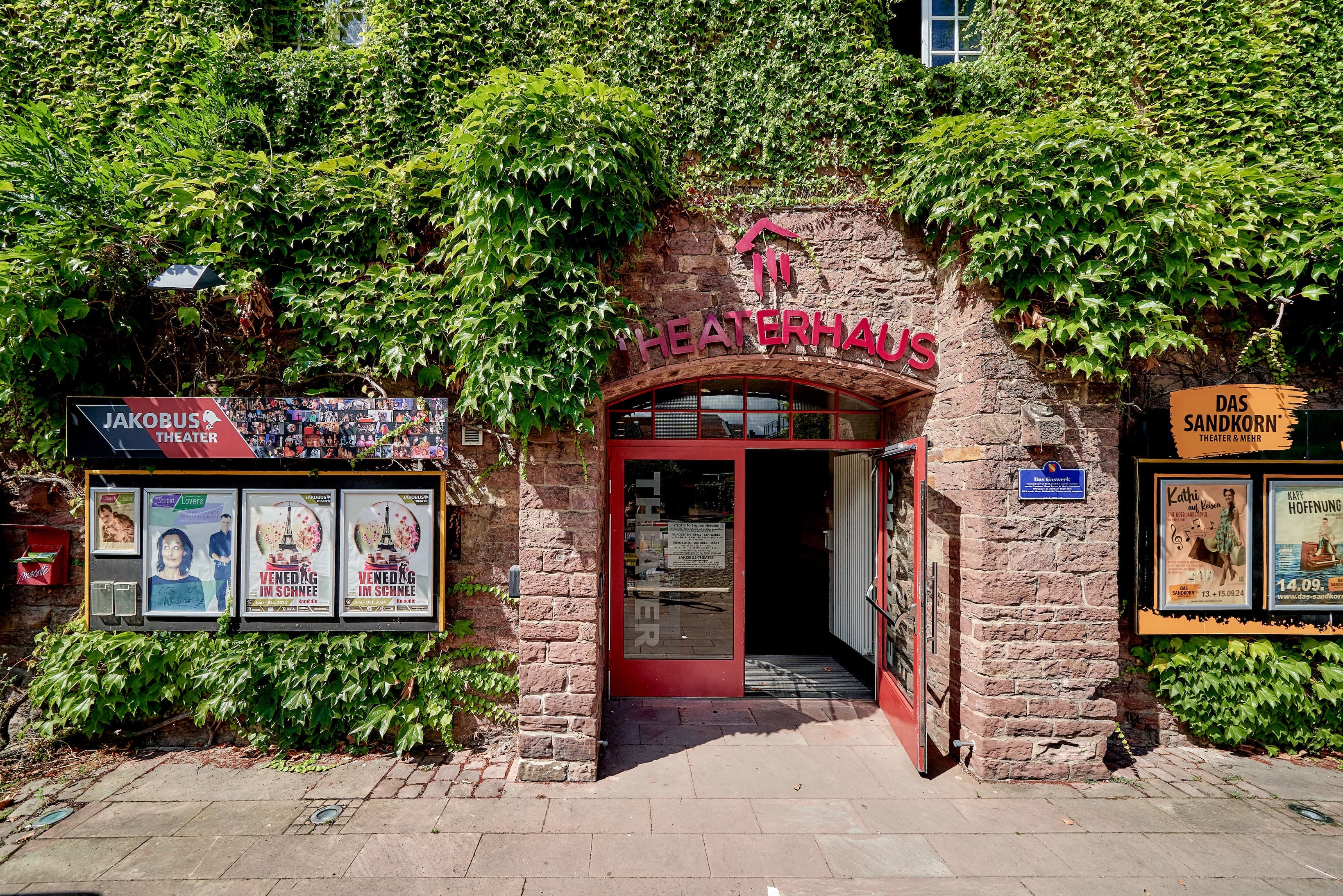 Blick auf den Eingang des Theaterhauses Karlsruhe mit Schriftzug über dem Eingang und das Gebäude bewachsen mit Efeu