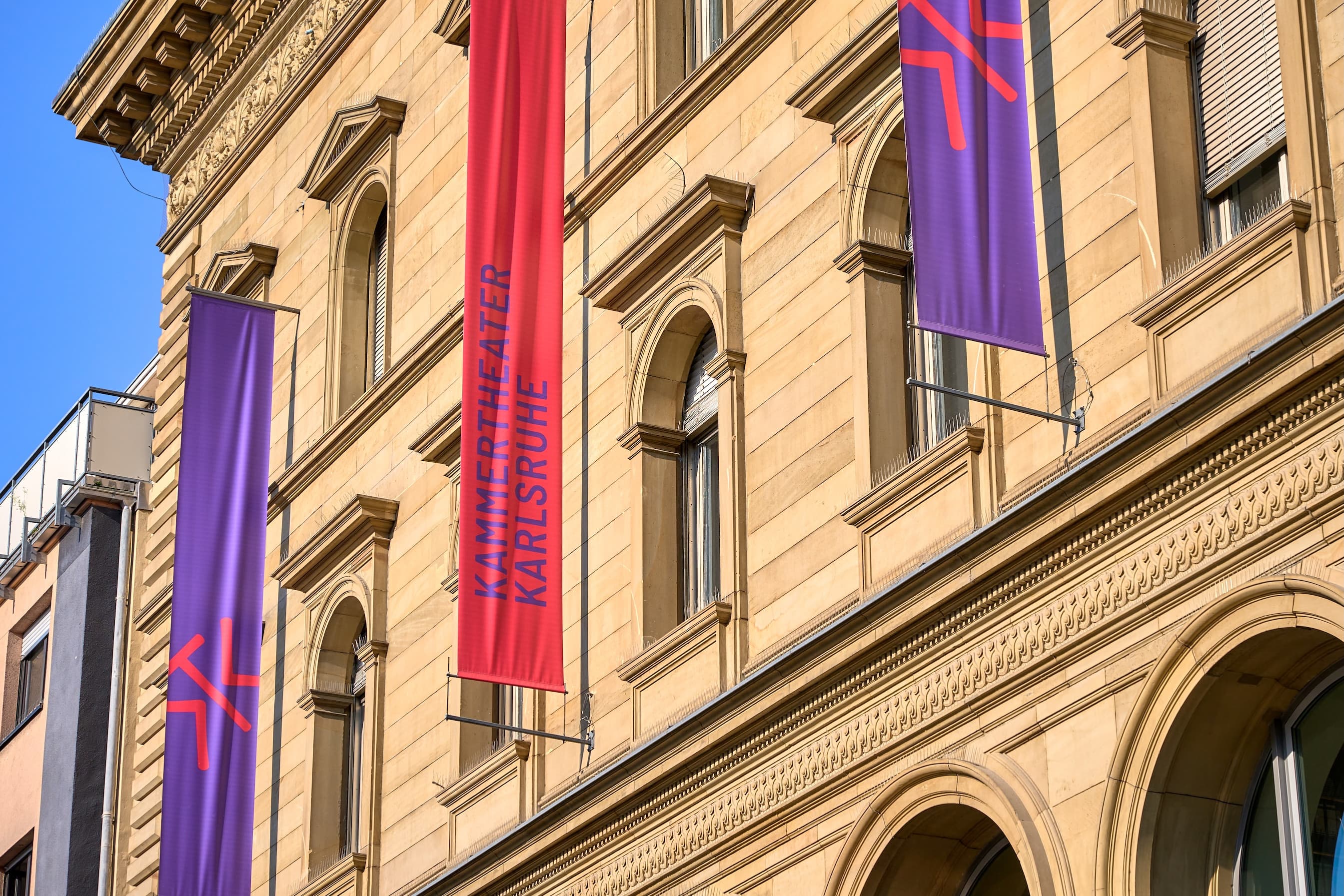 Fahnen am Gebäude des Kammertheaters Karlsruhe in Rot und Lila mit dem Logo des Kammertheaters
