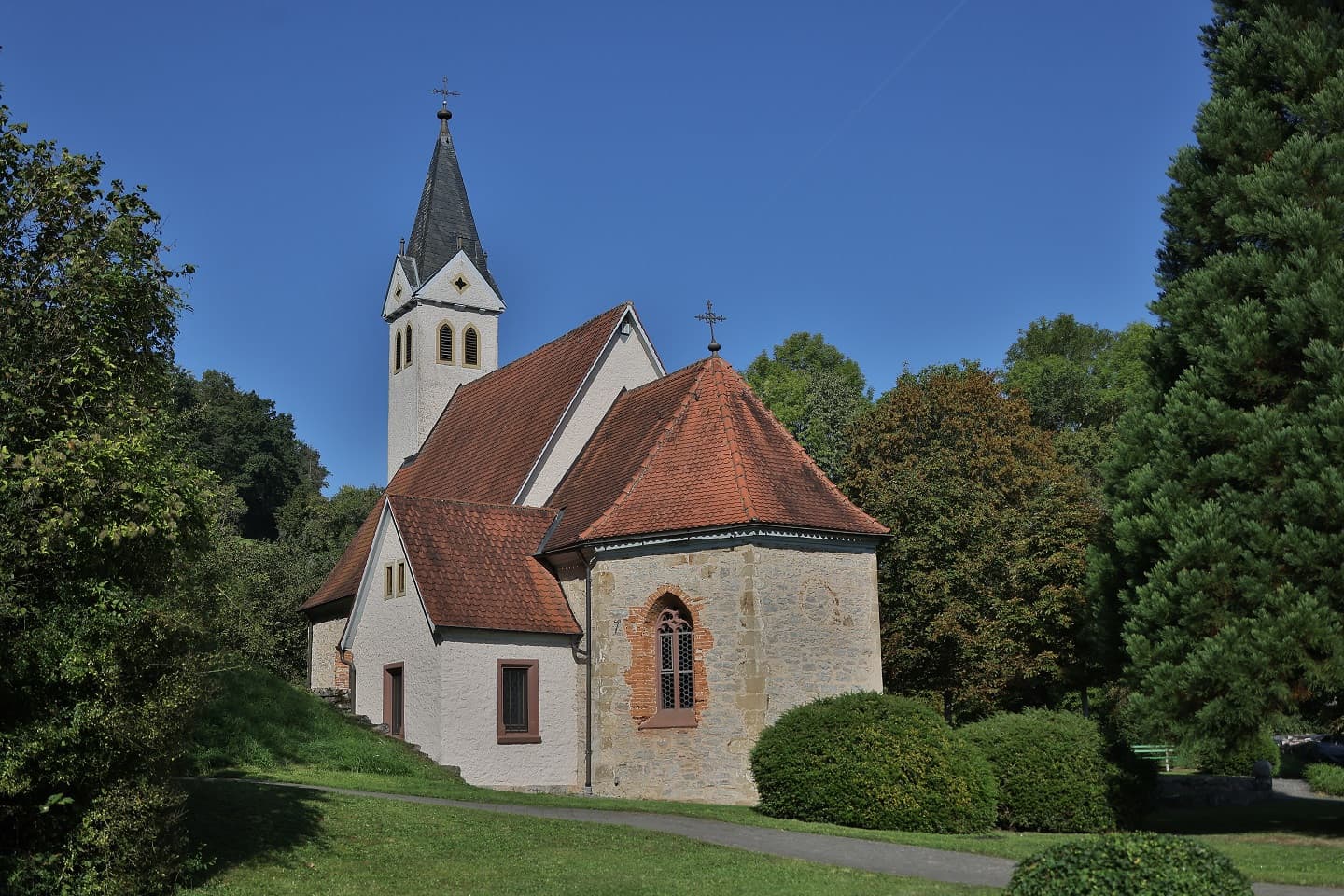 Die Kirche hat einen spitzen Turm und ist von grünen Bäumen umgeben