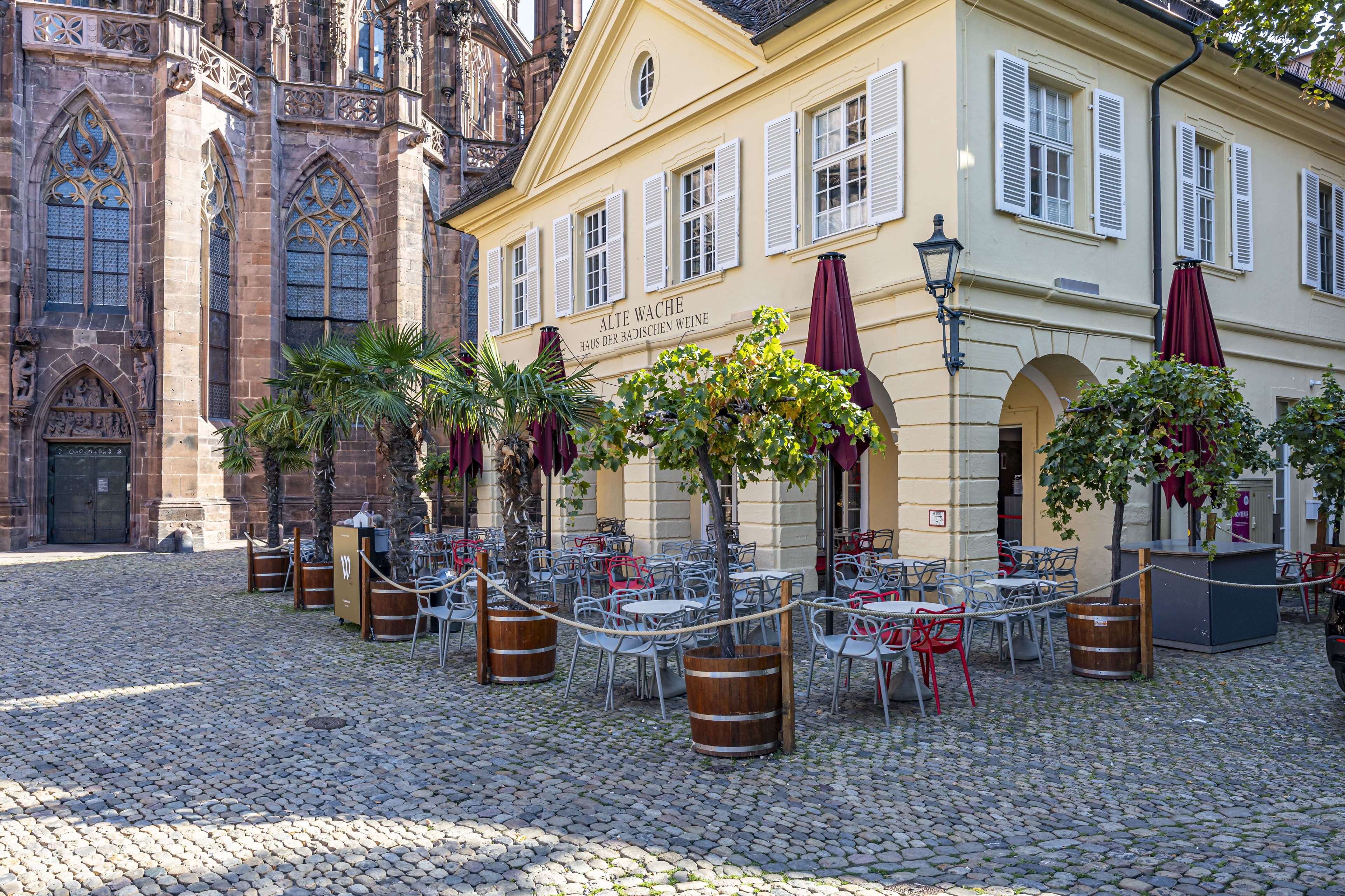 Außenansicht und Sitzbereich der Alten Wache, welche das Haus der badischen Weine beherbergt, mit Münster im Hintergrund