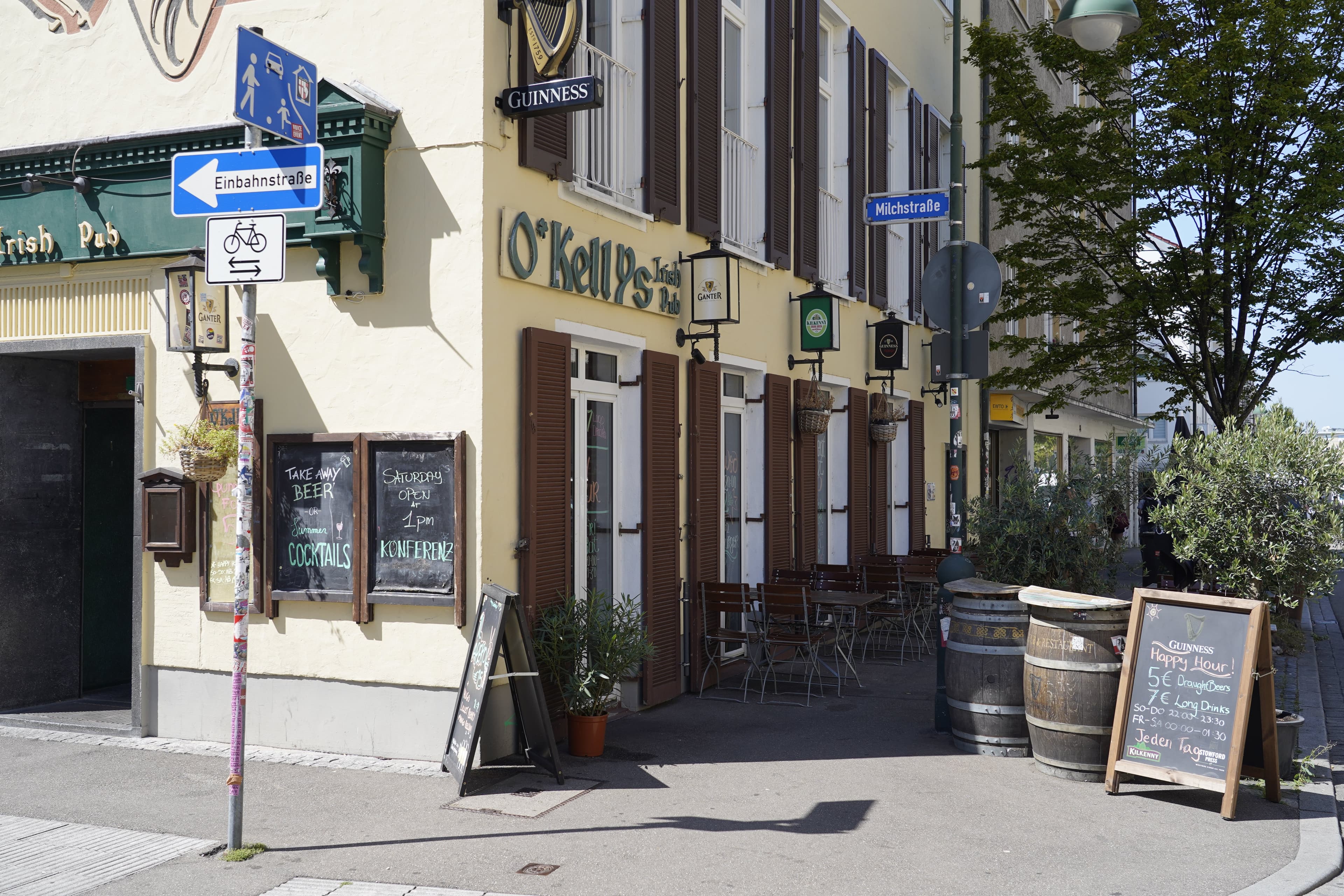 Außenansicht eines Irish Pubs mit Straßenschildern und Sitzgelegenheiten.