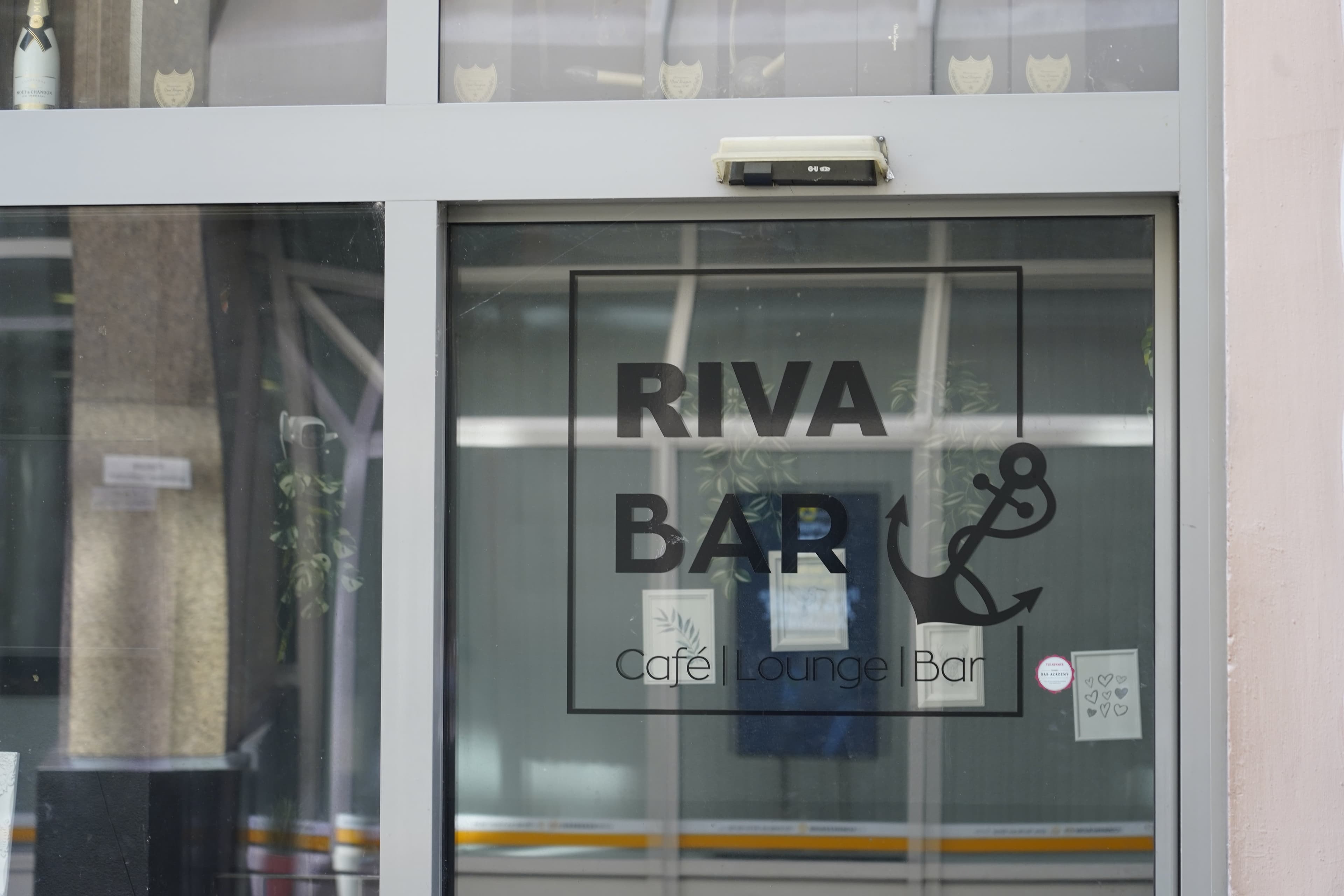 Eingang der Riva Bar mit Glasfront und Logo.