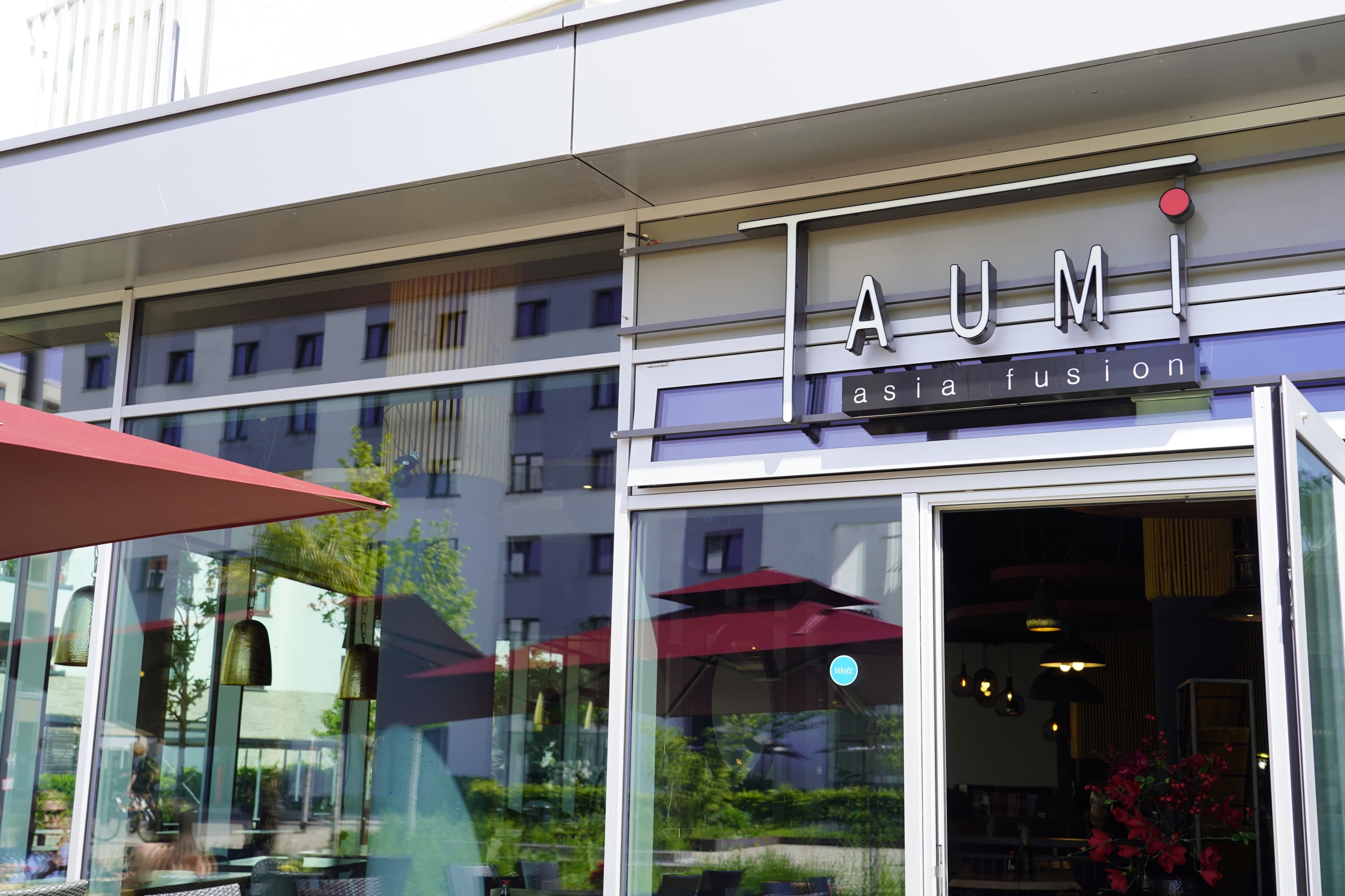 Eingang des Restaurants Taumi Asia Fusion in Freiburg mit geöffneten Türen und Spiegelung im Fenster.