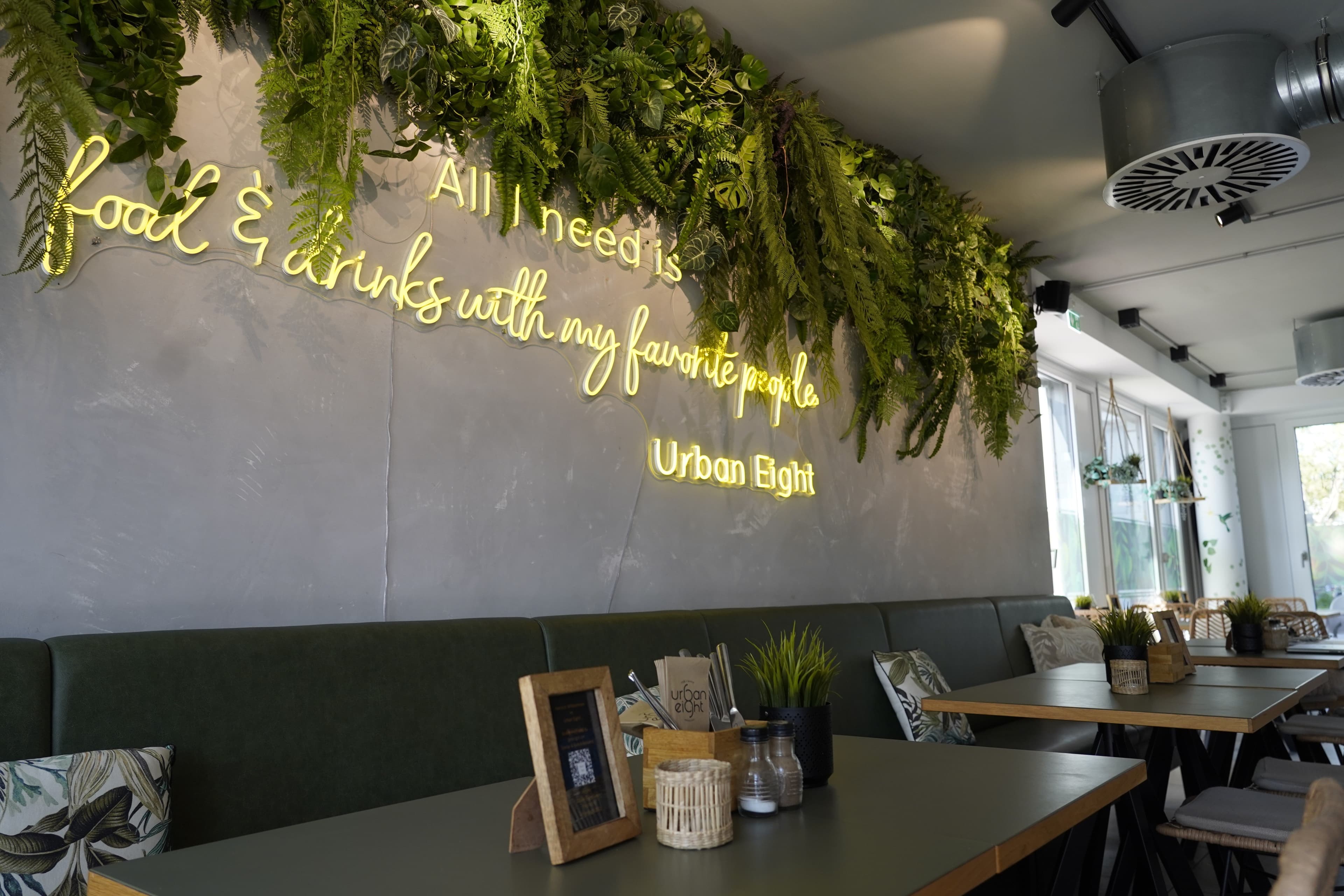 Innenansicht eines modernen Cafés mit grüner Dekoration und Neon-Schriftzug an der Wand.