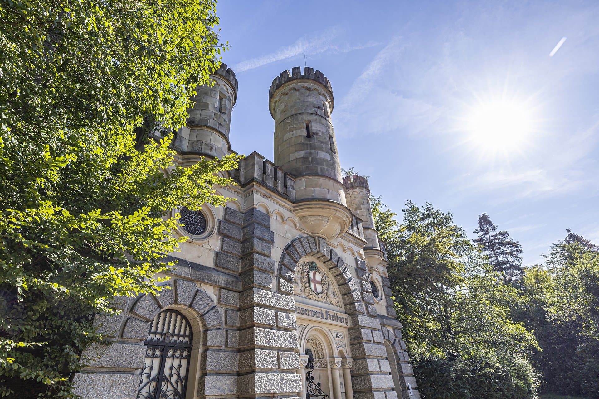 Schloss mit Bäumen nebendran, blauer Himmel und Sonne