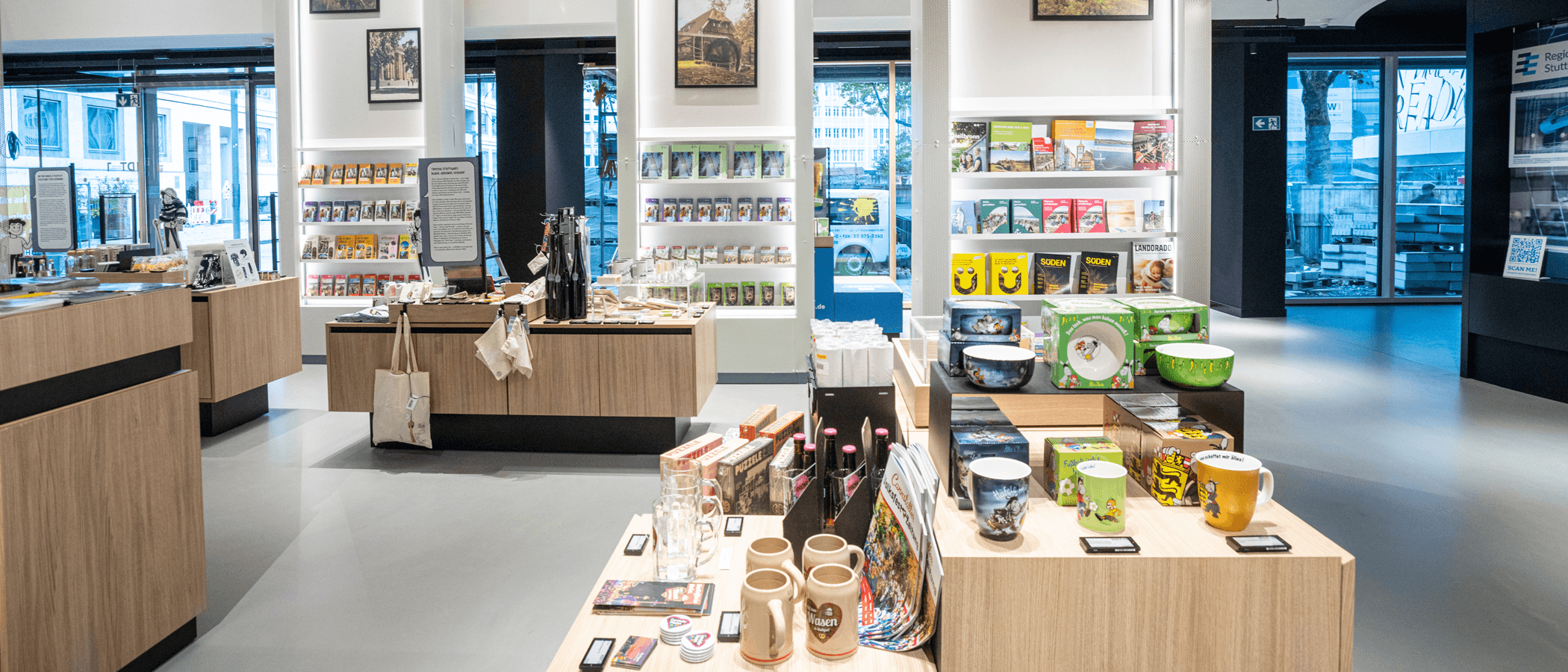 Innenansicht eines modernen Souvenirladens mit Regalen voller Bücher, Tassen und regionalen Produkten.