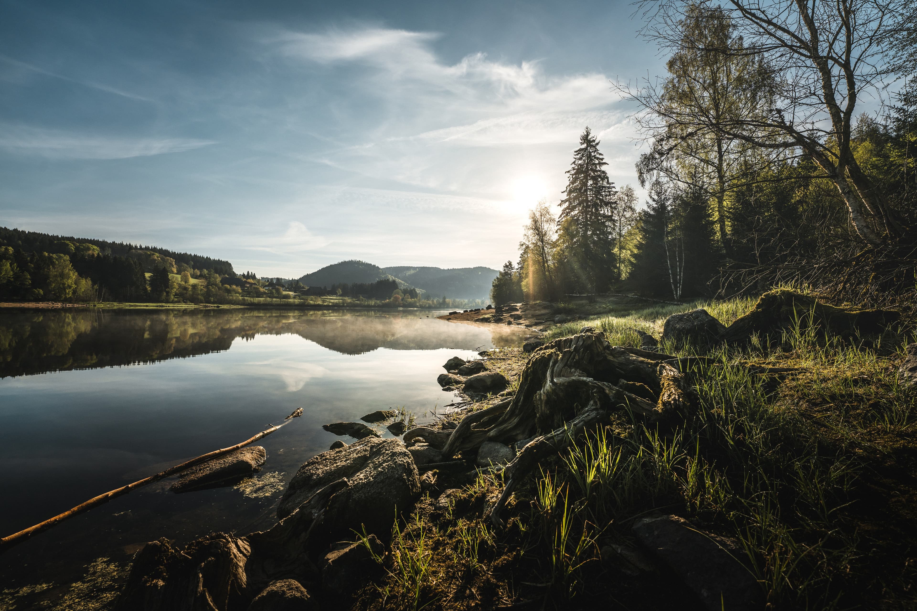 Naturlandschaft mit ruhigem See, Felsen und Bäumen, die sich im Wasser bei Sonnenaufgang spiegeln.