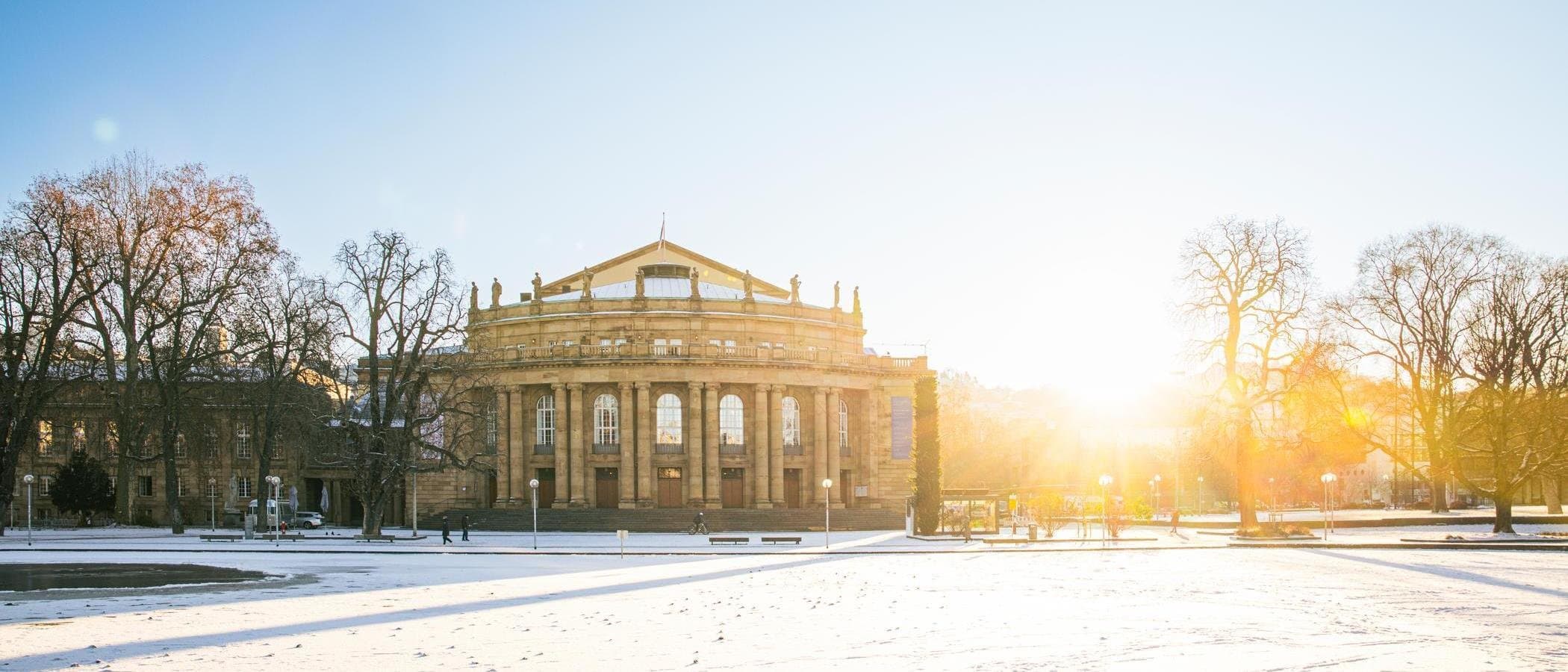 Die Stuttgarter Staatsoper im Winter mit schneebedecktem Boden und Sonnenaufgang im Hintergrund.