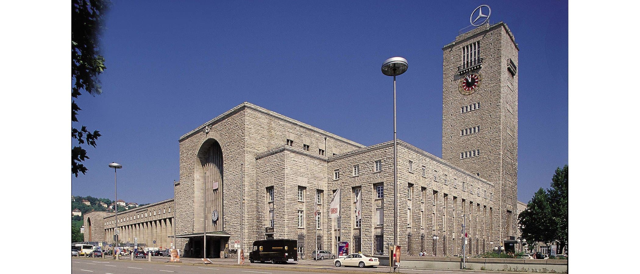 Hauptbahnhof Stuttgart mit Uhrturm und Mercedes-Stern vor blauem Himmel.
