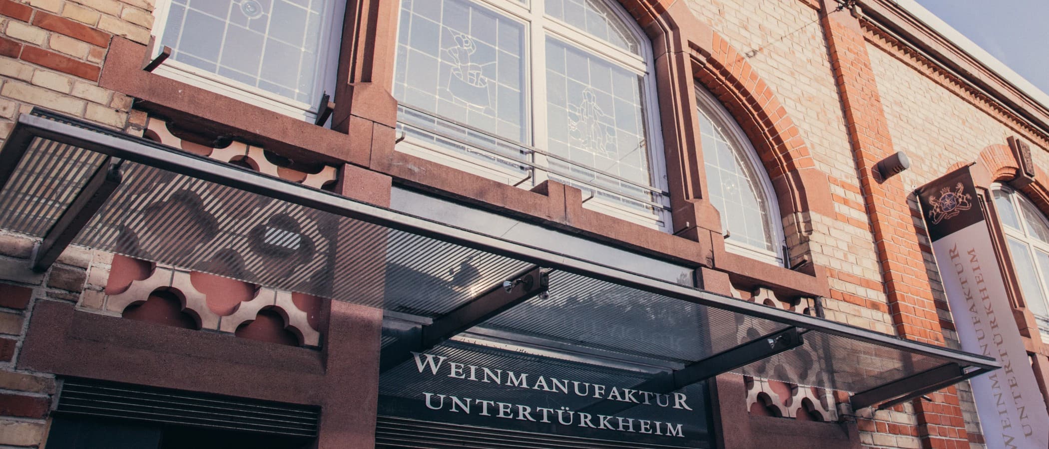 Fassade der Weinmanufaktur Untertürkheim mit Glasvordach und Schriftzug.