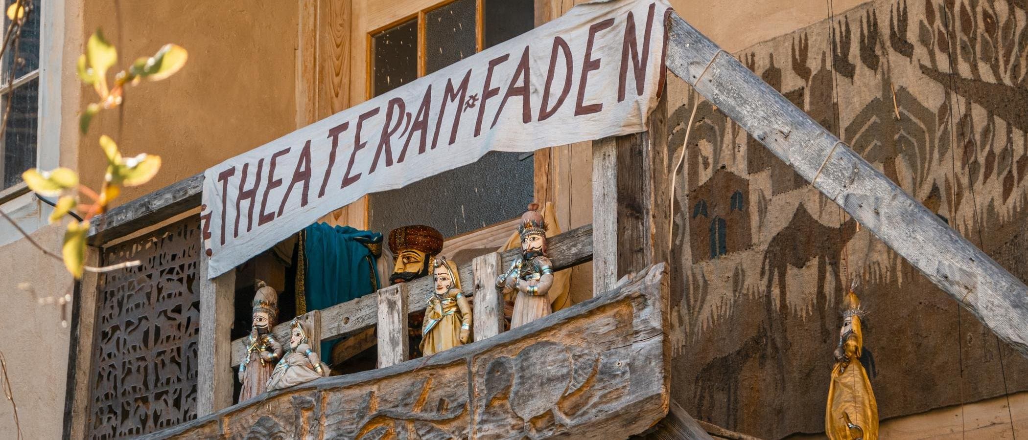 Holzbalkon mit Puppen und Banner 'Theater am Faden'.