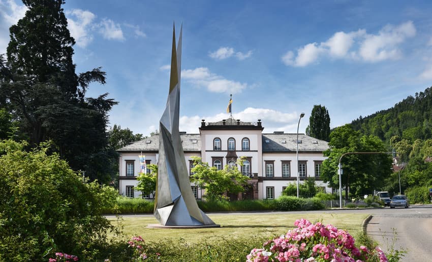 Daas Bild zeigt das Schloss in Schramberg sowie eine moderne silberne Skulptur von Erich Hauser, umgeben von einer schön bepflanzten Anlage