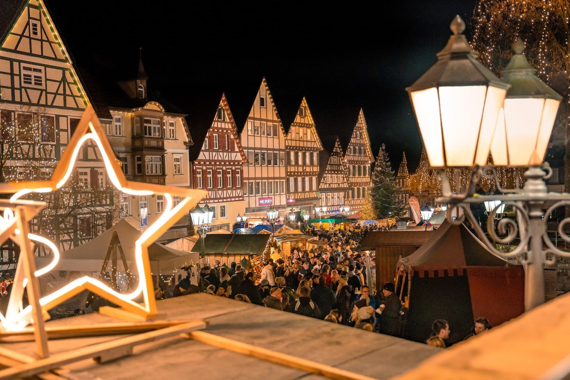 eine stimmungsvoll ausgeleuchtete Fachwerk-Kulisse eines Weihnachtsmarktes mit Ständen und Besuchern