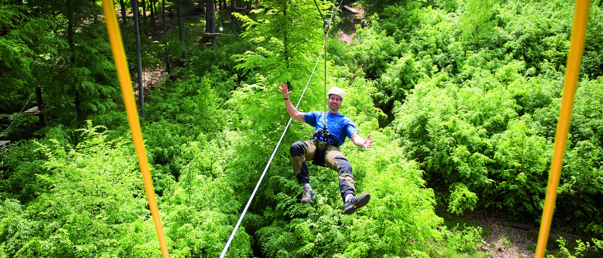 Person schwebt an einem Seil über einem grünen Wald im Kletterwald Plochingen.