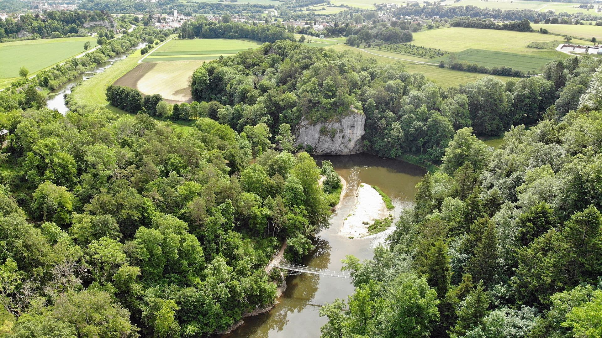 Luftaufnahme eines Flusses, der durch einen bewaldetes Gebiet um einen Felsen herum fließt